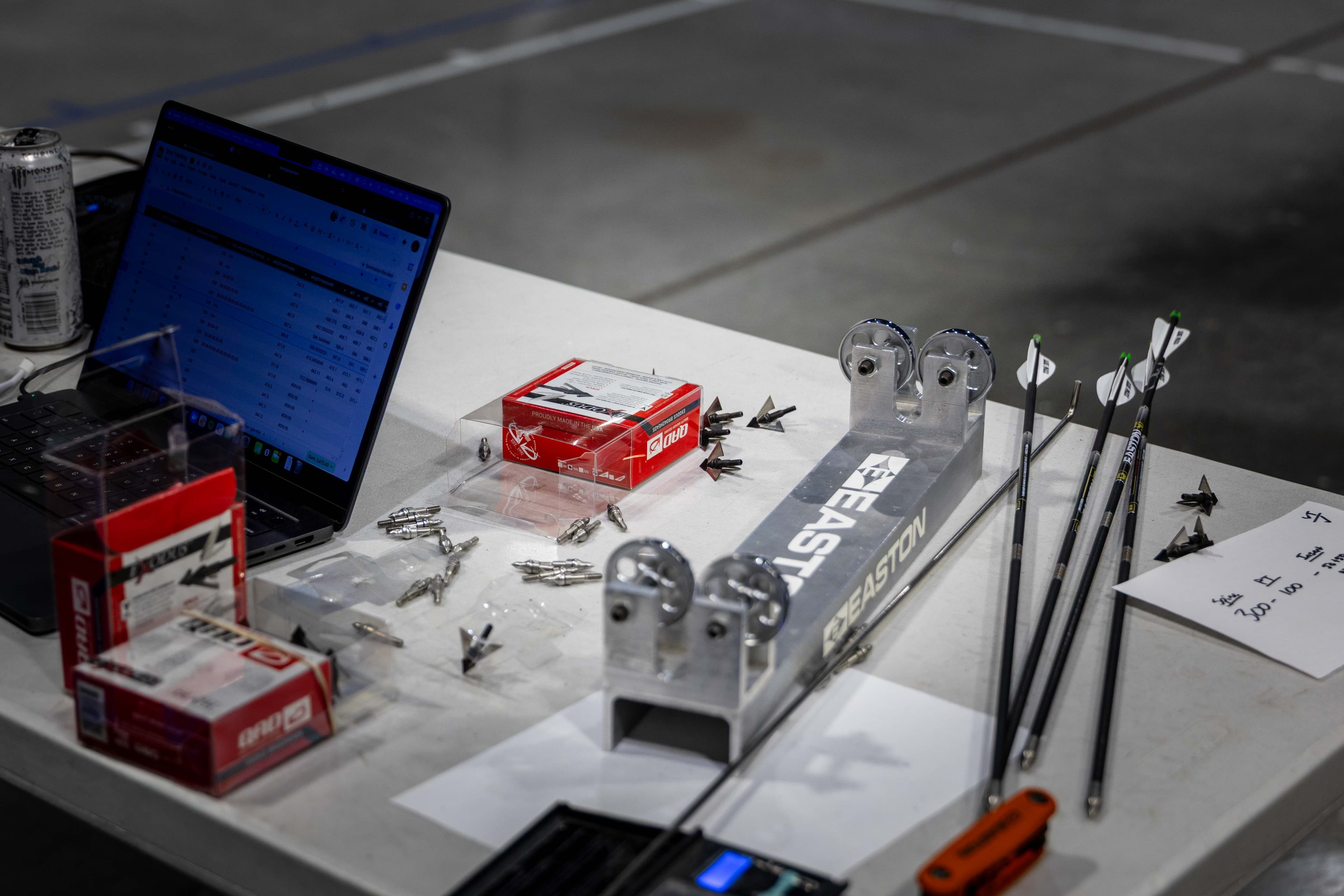 Workspace at the lab with laptop, broadhead components, and arrow weighing rest